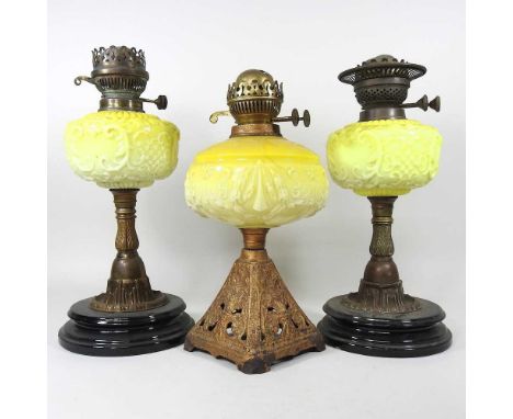 An early 20th century brass oil lamp, with a yellow opaque glass reservoir, 37cm high, together with two others (3)