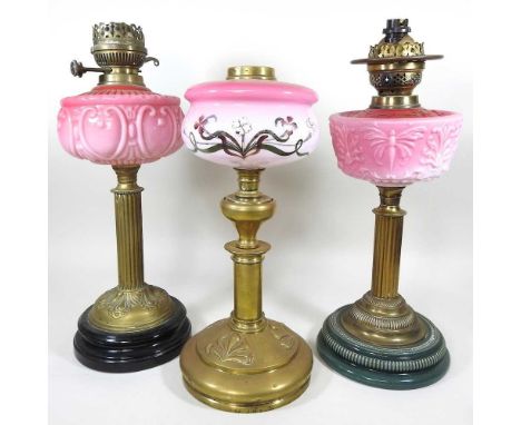 An early 20th century brass oil lamp base, with a pink glass reservoir, 47cm high, together with two others (3)