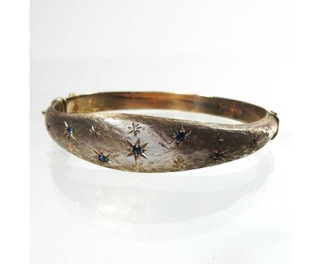 A 9 carat gold and sapphire bangle, of hinged design, with star decoration and offset with sapphires, with safety chain, 15.4