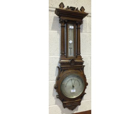 An Edwardian carved oak-cased barometer and thermometer, the 20cm diameter dial with Arabic numerals and a thermometer flanke