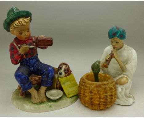 A Goebel figure of a boy attending to a sick dog and a Staffordshire figure of a snake charmer (2)