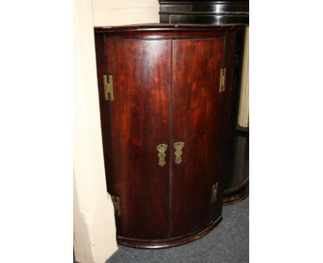 A George III mahogany bow front hanging corner cupboard with three shelves enclosed by two panel doors with brass 'H' hinges,