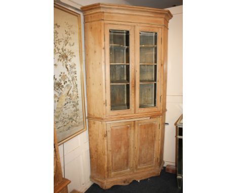 A pine corner cupboard with three shelves enclosed by two panel glazed doors above a cupboard, on shaped bracket base, approx