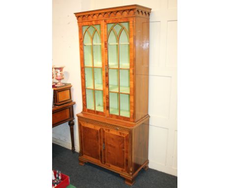 A 20th century yew wood bookcase with three shelves enclosed by twin glazed panel doors, on base with pull-out slide and cupb