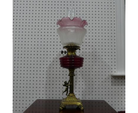 An antique brass columnar Oil Lamp,&nbsp;adorned with figure of Cupid and red glass reservoir, 63cm tall. 