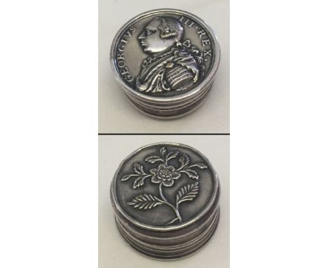 A small white metal patch/pill box.  Double sided with George III on one side and a floral decoration to the other.