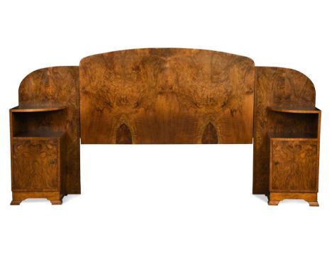 An Art Deco walnut bed head,  the arched headboard flanked to either side by a bedside cabinet, each with open shelf and cupb