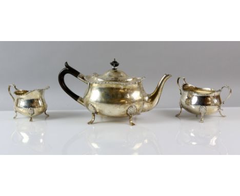 George V silver three piece tea service, comprising tea pot, cream jug and sugar bowl, with gadrooned borders on shaped feet,