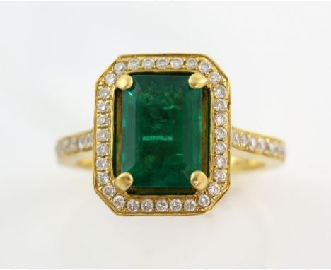 Emerald  and diamond set ring, the step cut stone of vibrant colour  in claw setting within a border of diamonds, diamond set