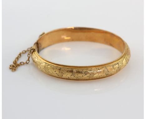 Early 20th C babies oval hinged bangle, with floral engraving and safety chain, in yellow metal testing as 15 ct .   Gross we