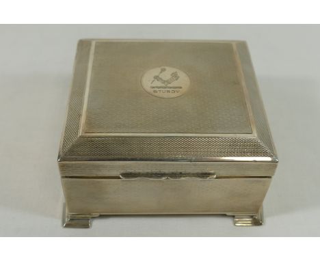 A George V square silver cigarette box, Chester 1921, with engine turned decoration and bearing armorial crest, with gilt int