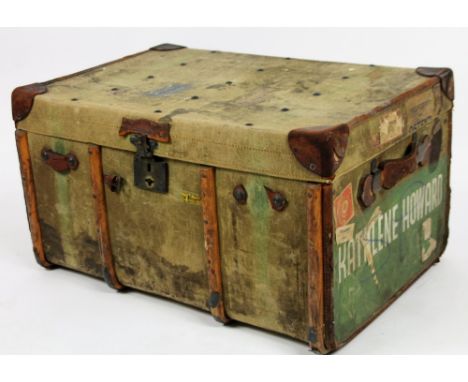 An early 20thC canvas trunk, partially wooden bound with leather extremities and handles, with luggage labels and part fitted