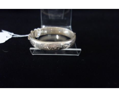 A SILVER BANGLE, with engraved decoration and safety chain