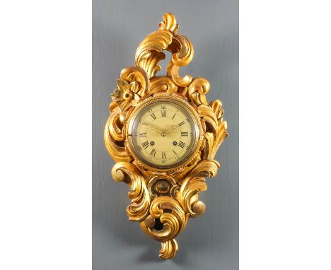 A 20th Century Continental carved giltwood cased cartel clock, the 6.5ins diameter domed metal dial with Roman and Arabic num