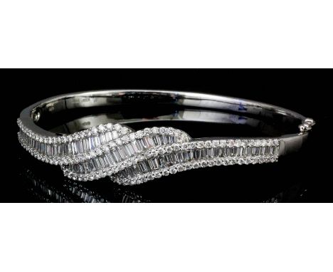 A modern 18ct white gold and diamond set stiff pattern bangle, the face with three swirling curves channel set with sixty-eig