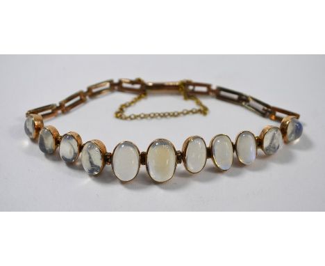 A yellow metal bracelet set with graduated oval cabochon moonstones, with gate-style links, fitted with safety chainApprox. 1