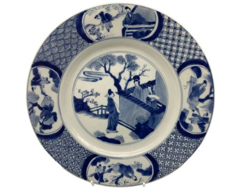 Chinese Kangxi plate decorated in blue and white with a figure looking over a wall with two figures in a garden, the border w