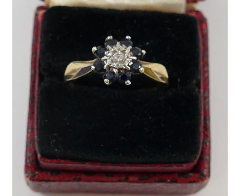 A 9 carat gold sapphire and diamond flower head cluster ring, London 1978, the central round brilliant cut diamond in illusio