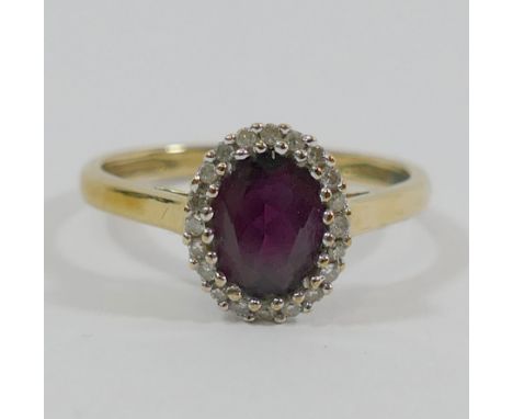A 9 carat gold oval almandine garnet and diamond cluster ring, Birmingham 2005, the oval mixed cut garnet within small eight-