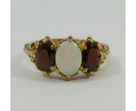 A 9 carat gold Victorian style opal and garnet three stone ring, London 1975, the oval cabochon opal claw set between two mix