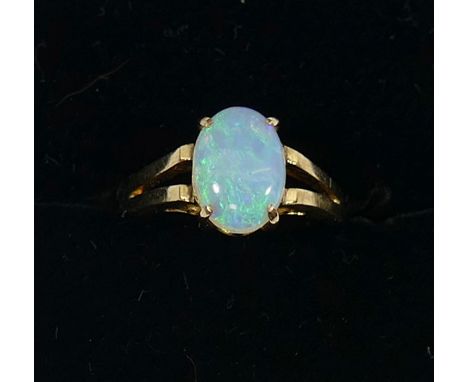 A yellow metal opal single stone ring, the oval opal cabochon in four claw setting between split shoulders, the shank stamped