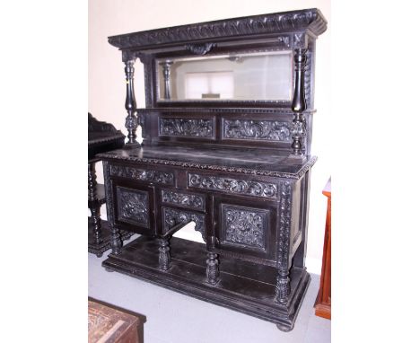 A late Victorian ebonised carved oak dresser with mirror panel back over three drawers, cupboards and under-tier, on bun feet