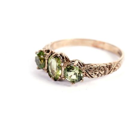 A three-stone peridot ring, in 9ct yellow gold mount, and shank with scrolling shoulders, ring size O, 2.1g gross.