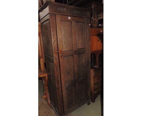 An oak hall robe in the Old English style enclosed by a full length panelled door within a panelled frame with carved frieze,