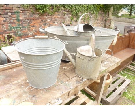 A galvanised 2-handled bath of oval form, two galvanised watering cans of varying capacity, a bucket with loop handle and a b