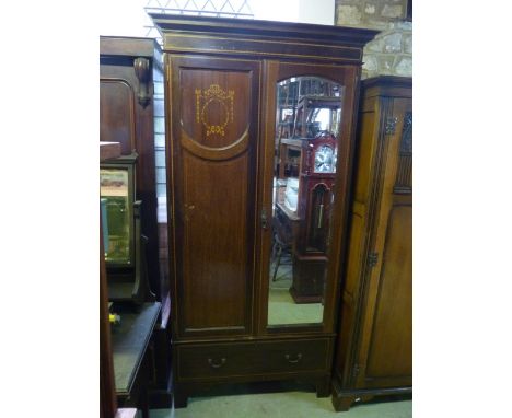 An inlaid Edwardian mahogany wardrobe with moulded cornice over a pair of threequarter length panelled doors, one with arched