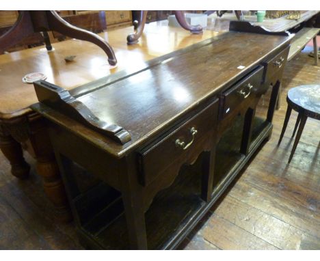 A Georgian oak cottage pot board dresser base enclosed by three frieze drawers over a shaped apron and lower shelf, 155 cm lo