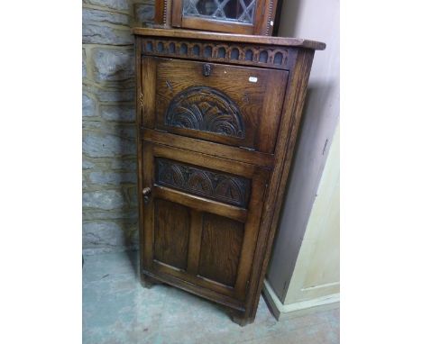 A reproduction oak freestanding corner cupboard enclosed by a triple panelled door and fall front with carved foliate detail,