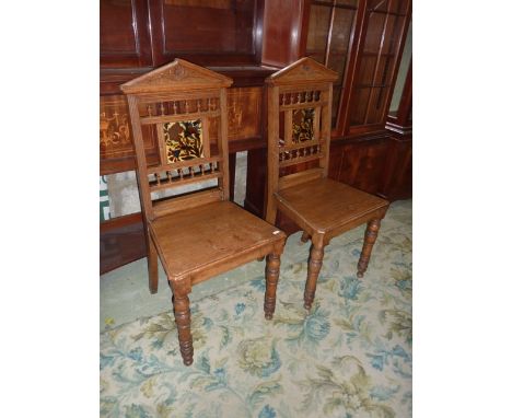 A pair of late Victorian oak hall chairs, the raised architectural backs with carved foliate and moulded rails, the turned ga