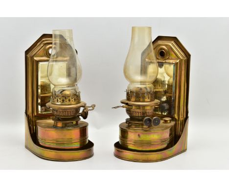 A PAIR OF LATE VICTORIAN BRASS WALL HANGING OIL LAMPS, the shaped rectangular raised back fitted with a bevel edged mirror, t