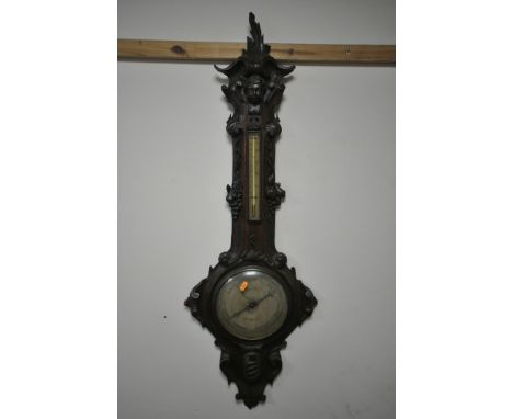 A VICTORIAN OAK WHEEL BAROMETER, the frame with a carved mask of a boy, and leaf scrolls and fruiting vines surrounding a the