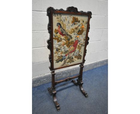AN EARLY VICTORIAN ROSEWOOD FIRESCREEN, the frame with foliate scrolls, the glass panel enclosing needlework depicting two pa