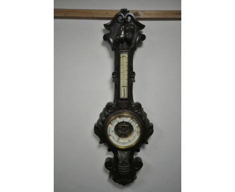 A LATE 19TH/EARLY 20TH CENTURY CARVED OAK ANEROID BAROMETER, with a thermometer, the frame carved with exotic fruits and foli