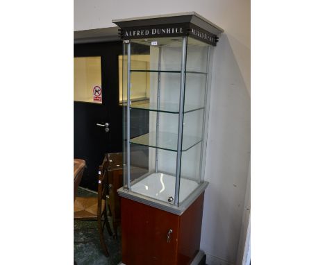 An Alfred Dunhill free standing display cabinet, glass shelves to top, cupboard to base. 196cm high x 55cm square.