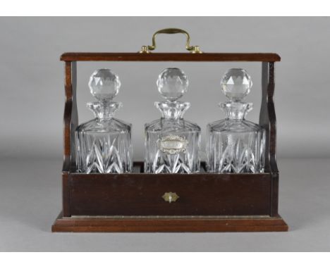 A mahogany and brass three bottle tantalus with three Edinburgh crystal square cut decanters with ball stoppers, one decanter