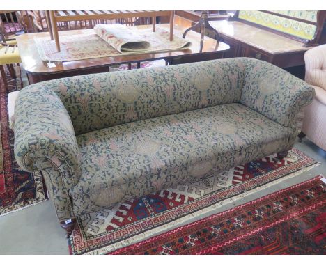 A Victorian Chesterfield style sofa with foliate upholstery, scroll arms upon turned mahogany feet terminating on ceramic cas