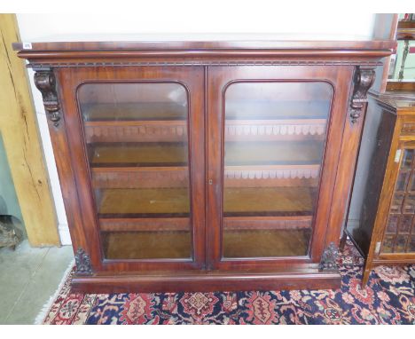 A Victorian flame mahogany glazed bookcase with moulded top having scroll and finial supports, twin cupboard doors having arc