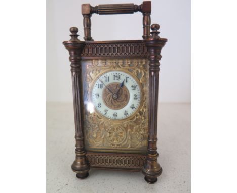 A French brass carriage clock with brass spandrels surrounding white enamel chapter ring with Arabic numerals, bevelled glass