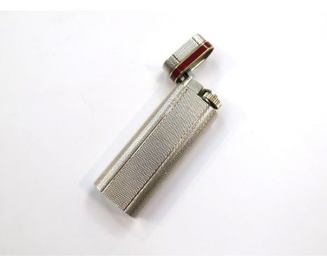 A Cartier white metal cigarette lighter, engine turned casing with red enamel and gilt metal band, 7cm long