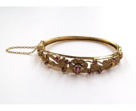 A gold bangle set with rubies, floral and foliate pierced design, unmarked, 14.8g