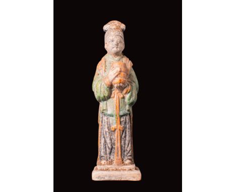 Ca. AD 1368 - 1644 or later.A pottery figure portraying a female attendant standing on an integral two-stepped base, clad in 