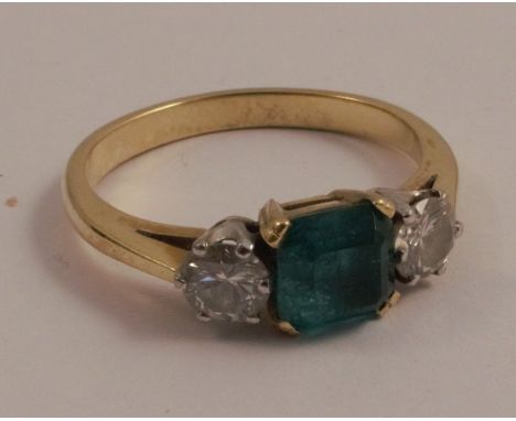 An emerald and diamond three stone ring, unmarked, the square step cut stone flanked either side by brilliant cuts totalling 