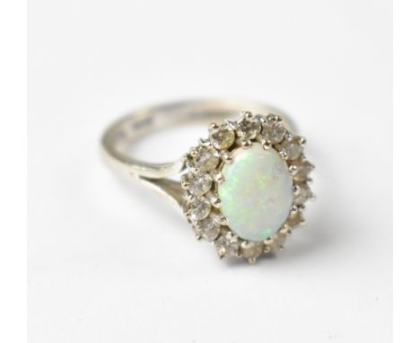 An 18ct white gold opal and diamond ring, the central oval claw mounted opal with green and blue speckles, within a halo of f