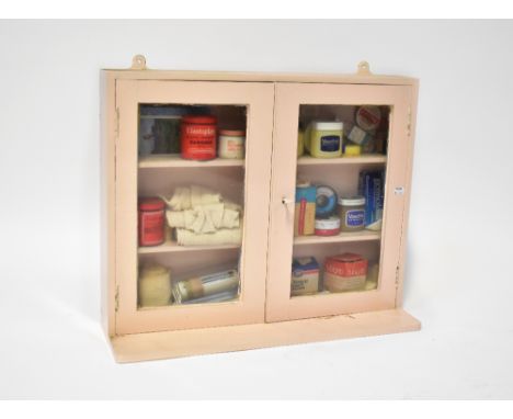 A mid-20th century pink painted wooden wall-hanging First Aid cabinet with two glazed doors, containing a quantity of First A