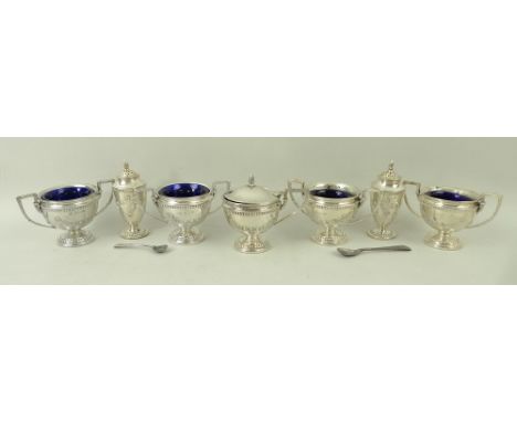 A seven piece silver cruet set decorated with embossed garlands and beading, comprising four table salts of urn form with two