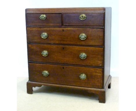 A George III oak chest of two over three drawers, with caddy top and brass embossed oval plate handles, raised on shaped brac